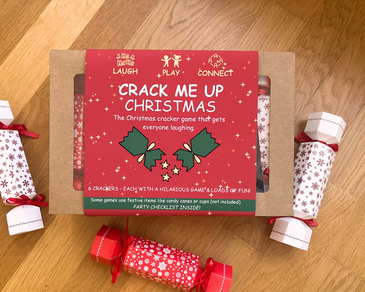 Crack Me Up Christmas cracker game box on wooden background with crackers around the box