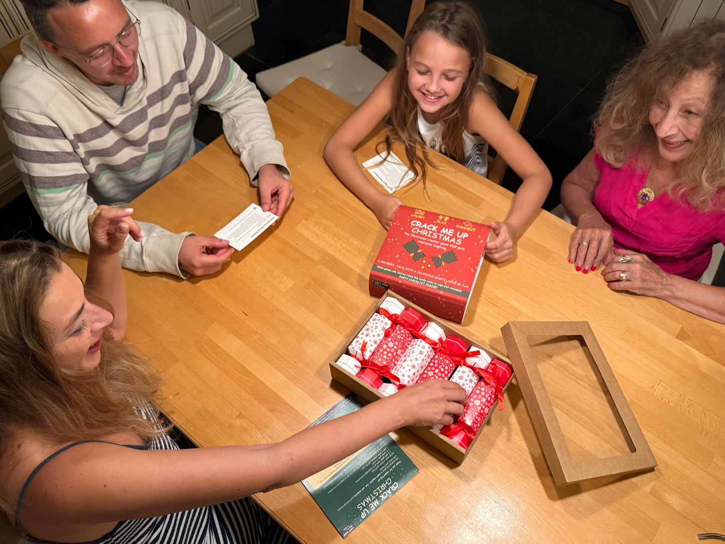 Family gathered around a table with Crack Me Up Christmas party game in the middle..